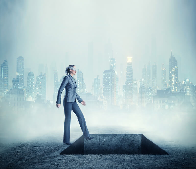 Businesswoman blindfolded standing near a deep pitfall in the town