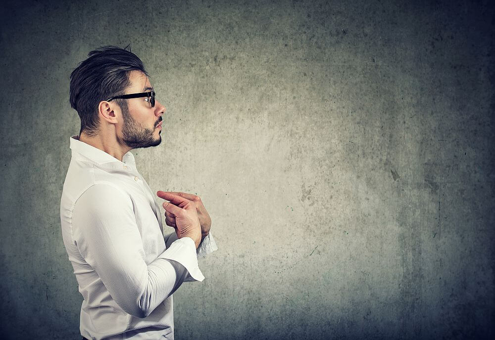 Shocked businessman pointing at himself being in denial against gray background